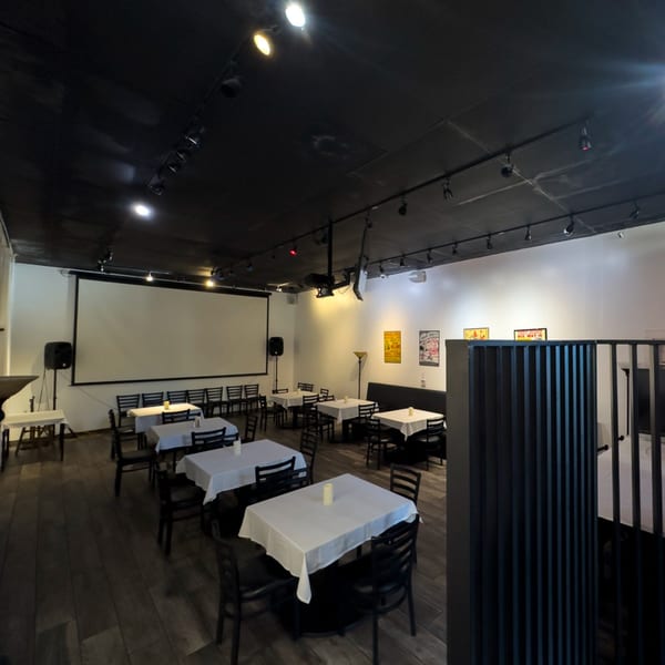 Dining room at Pizzeria Vivoli & Italian Grill with white-clothed tables, dark chairs, and a large projection screen.