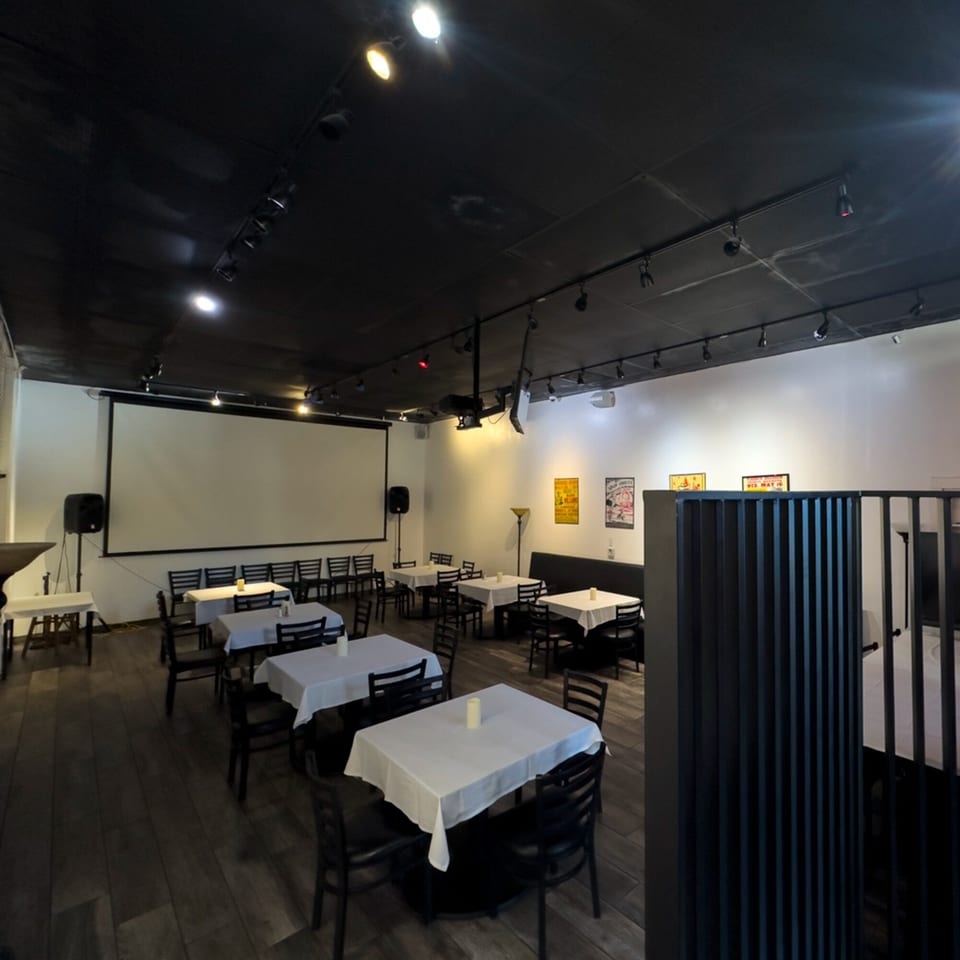 Dining room at Pizzeria Vivoli & Italian Grill with white-clothed tables, dark chairs, and a large projection screen.