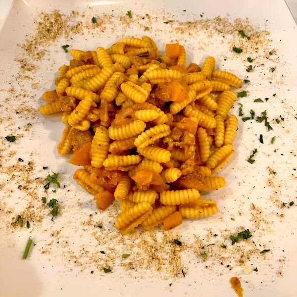 A plate of cavatelli pasta with a rich orange sauce, garnished with herbs and spices.