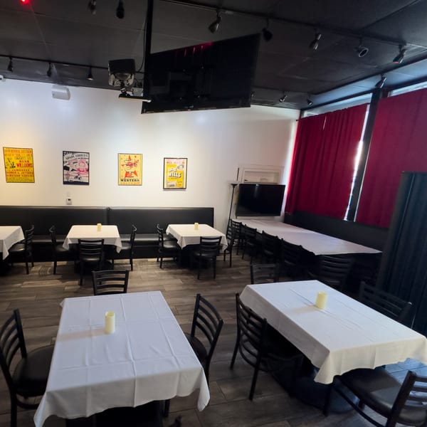 Empty dining room at Pizzeria Vivoli with white tablecloths, black chairs, and vintage posters on the wall.