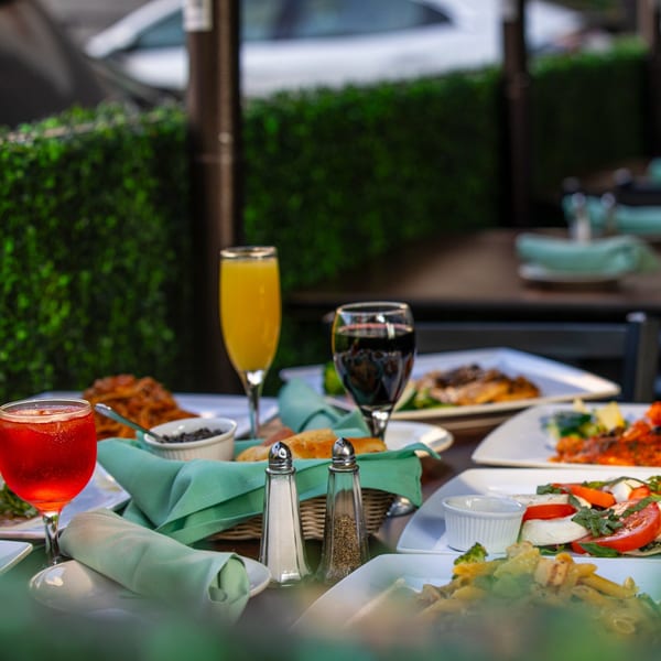 Outdoor dining table at Pizzeria Vivoli with Italian dishes, drinks, and green hedges in the background.