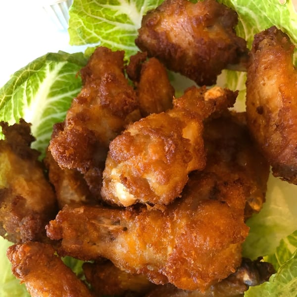 Crispy fried chicken wings, golden brown and piled on a bed of fresh green lettuce.