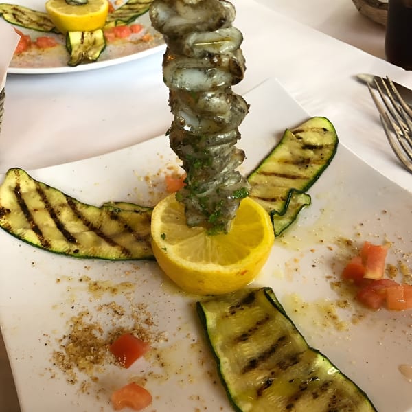 Grilled shrimp skewer on a lemon half, surrounded by grilled zucchini slices and diced tomatoes.