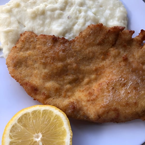 Crispy fried chicken cutlet with a side of mashed potatoes and a lemon wedge.