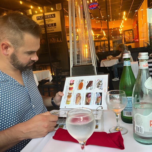 A man at Pizzeria Vivoli & Italian Grill reviews a dessert menu on an outdoor patio.