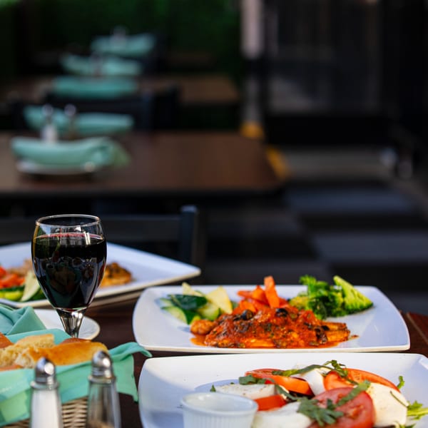 Italian dishes, including Caprese salad and a main course, with red wine on an outdoor table.