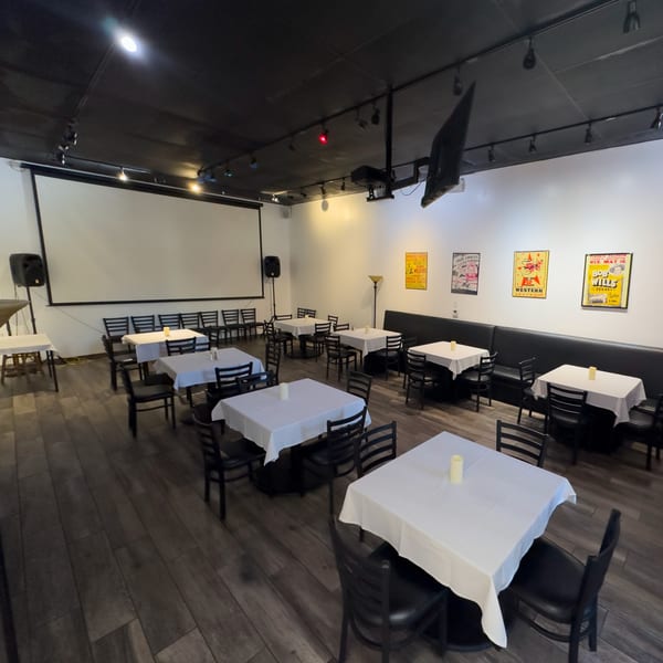 Pizzeria Vivoli's dining room with white-clothed tables, black chairs, a projector screen, and vintage posters.