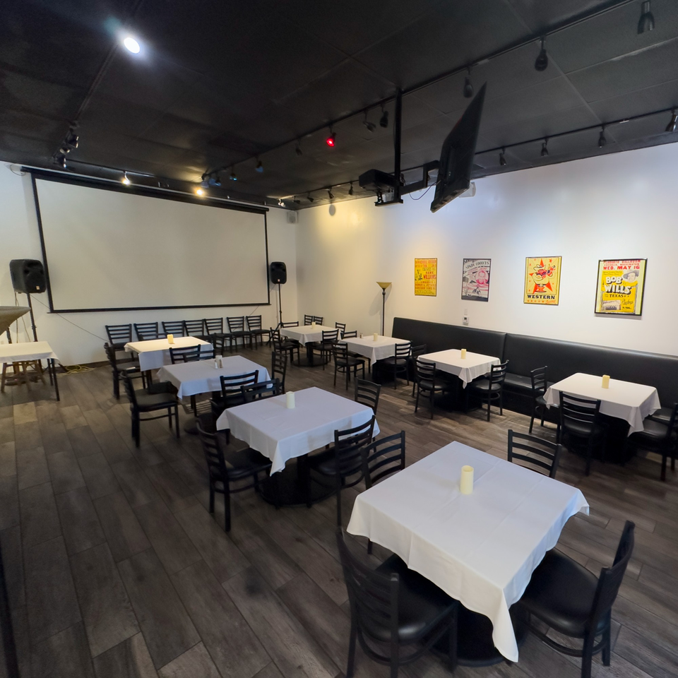 Pizzeria Vivoli's dining room with white-clothed tables, black chairs, a projector screen, and vintage posters.