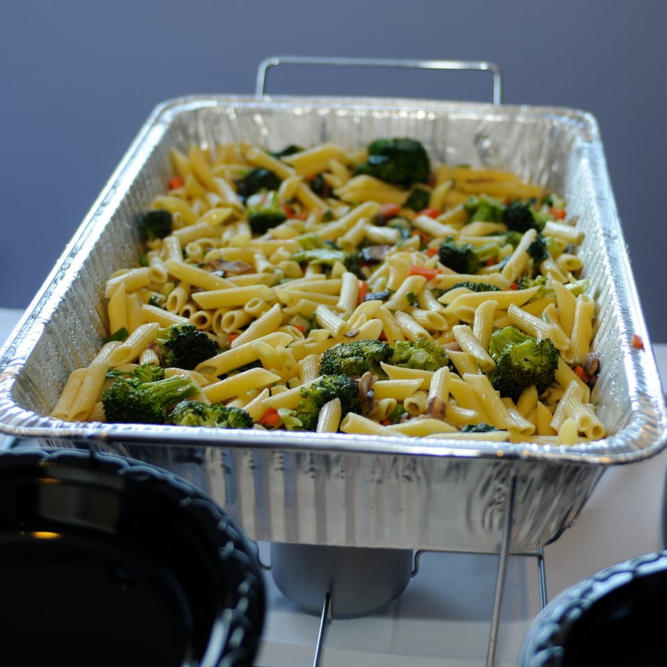 Penne pasta with broccoli and vegetables in a large aluminum catering tray.