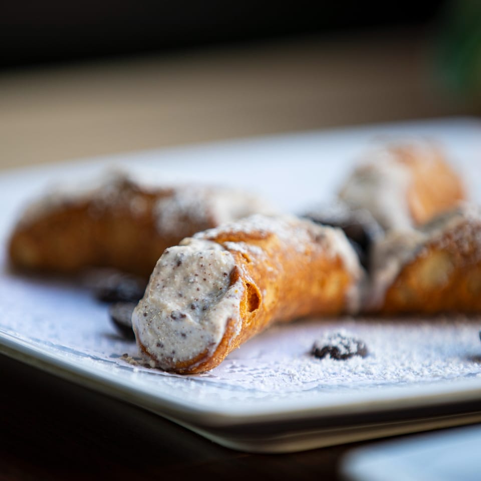 Three cannoli with creamy filling and powdered sugar on a white plate at Pizzeria Vivoli.