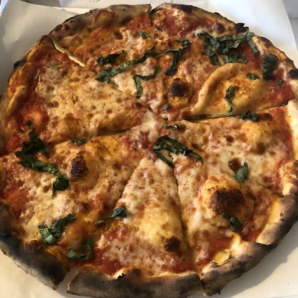 A freshly baked, sliced Pizzeria Vivoli pizza with melted cheese, red sauce, and basil.