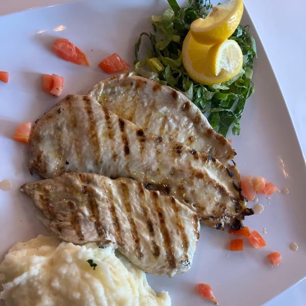 Grilled chicken breasts with mashed potatoes, a side salad, and lemon wedges on a white plate.