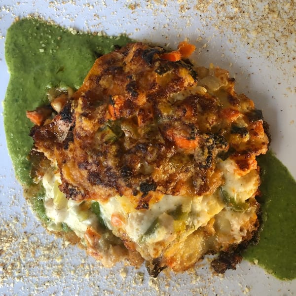 A golden-brown baked dish with vegetables and cheese, served on a green sauce with breadcrumbs.