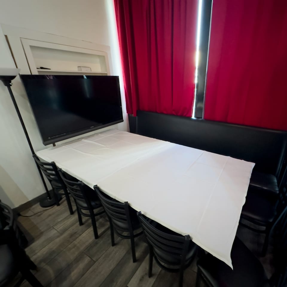 Long table with white tablecloth and black chairs, a TV, and red curtains at Pizzeria Vivoli.
