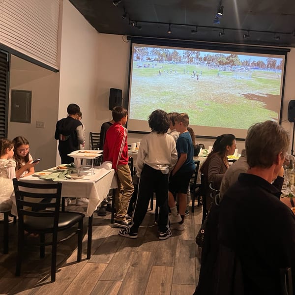 Diners at Pizzeria Vivoli & Italian Grill watching a soccer game projected on a large screen.