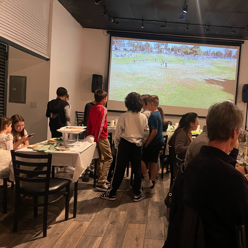 Diners at Pizzeria Vivoli & Italian Grill watching a soccer game projected on a large screen.