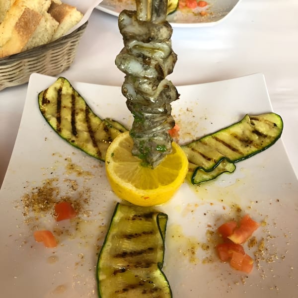 Grilled shrimp skewer with lemon and zucchini slices on a white plate at Pizzeria Vivoli.