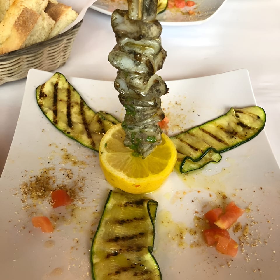 Grilled shrimp skewer with lemon and zucchini slices on a white plate at Pizzeria Vivoli.