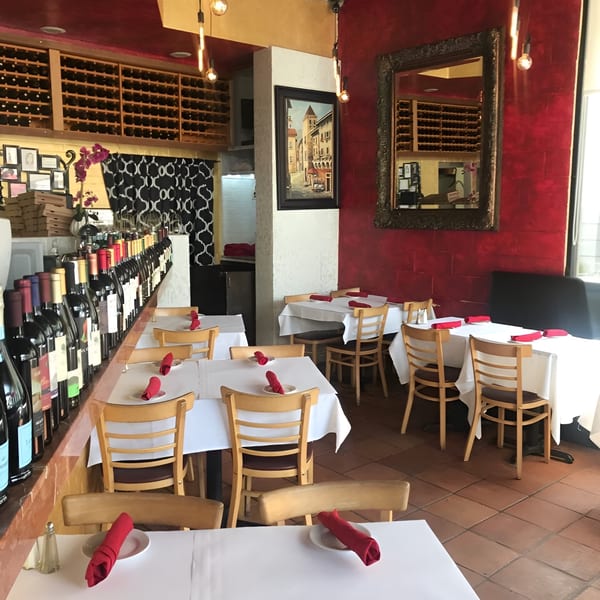 Interior of Pizzeria Vivoli & Italian Grill with set tables, wine bottles, and red walls.