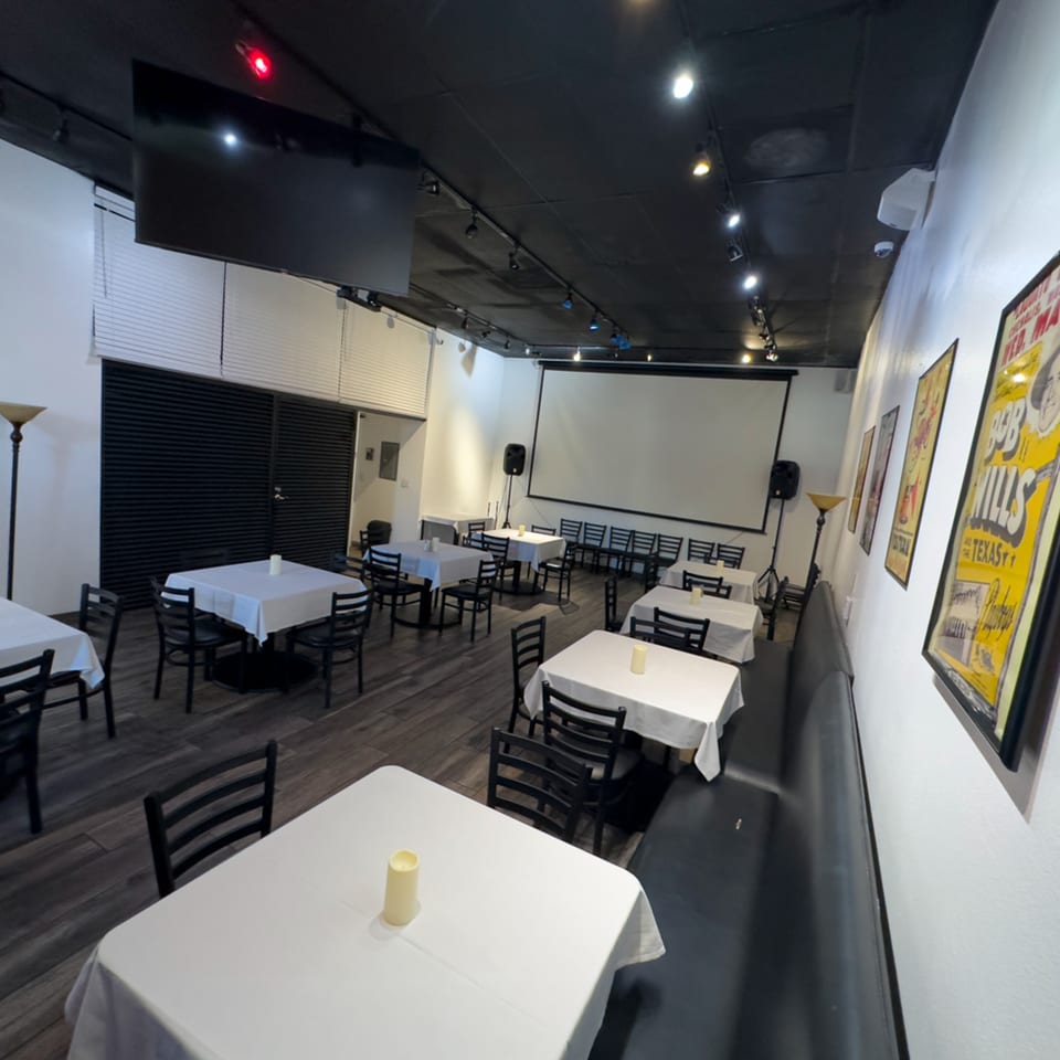 Pizzeria Vivoli's dining room with white-clothed tables, black chairs, a projector screen, and framed posters.